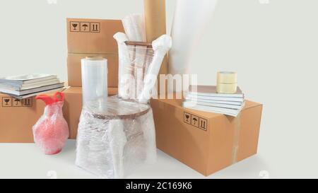 Moving scene with a chair and vase packed in plastic bubble with closed cardboard boxes, books and rolls of plastic and foam to pack on white backgrou Stock Photo