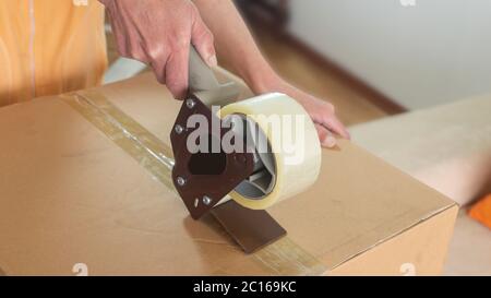Close up on a woman's hands closing a cardboard box with adhesive tape Stock Photo