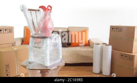 Moving scene with a vase on a chair on a table packed in plastic inside a room with a sofa, plastic rolls and closed cardboard boxes on white backgrou Stock Photo