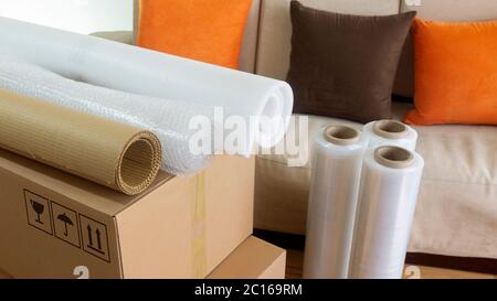 Approach to three rolls of cardboard, foam and bubble wrap used to pack things on a cardboard box with a sofa in the background Stock Photo