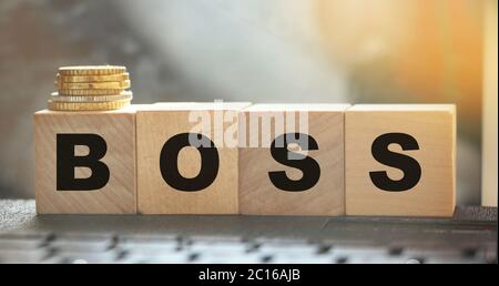 The boss sign on a wooden cubes standing on computer keyboard and stack of coins. CEO business management concept Stock Photo