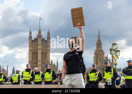 A Black Lives Matters protester holds up a sign in front of a line of police officers on Westminster Bridge, London, 13 June 2020 Stock Photo
