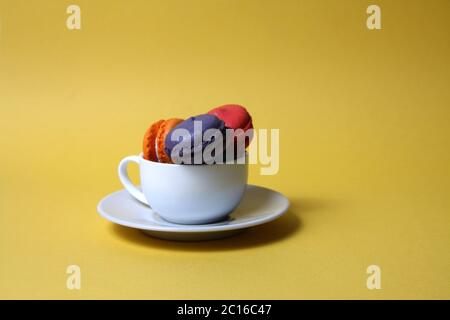 Macaroons of differrent colours in a tea cup isolated on yellow background. Image contains copy space Stock Photo