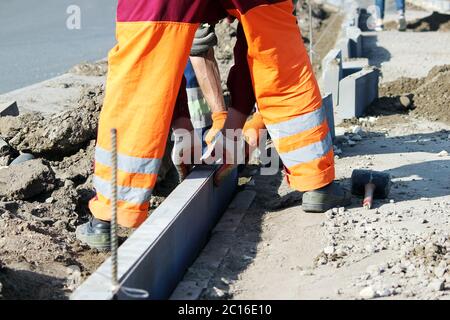 Repair of the sidewalk. Professional working masons in overalls lay curbs before laying stone paving slabs. Stock Photo