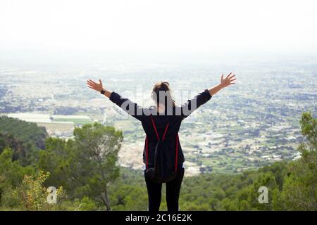Sportswoman reaches a mountain top and raises arms celebrating the achievement and success of her physical activity purpose. Stock Photo