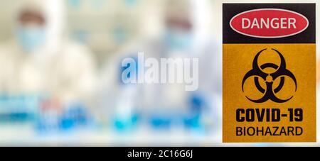 Panoramic Caution danger Signage of COVID-19 coronavirus in front of Laboratory room with background of Scientists working and researching vaccine for Stock Photo