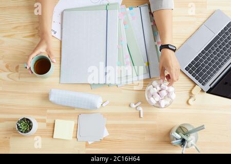Top down view of cute home office workplace with female hands holding coffee mug over wooden table, copy space Stock Photo