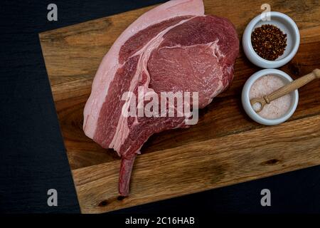 pork meat with bone on a wooden plate with salt and hot spices in small porcelain bowls Stock Photo