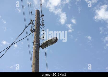 An old electric wooden pole with a lamp and electricity cables hanging on. Natural light. Stock Photo