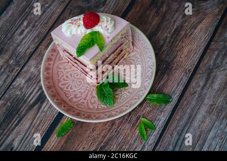 Tasty piece of raspberry multi-layered cake on plate. raspberry cake served for dessert on wooden background with mint leaves. Delicious slice tart on plate. Baking and decorating raspberry cake Stock Photo