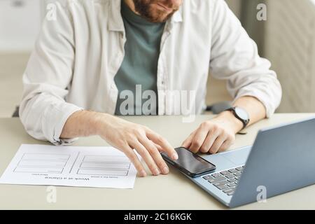 Cropped portrait of bearded young man using smartphone while working at home office in minimal light interior, copy space Stock Photo