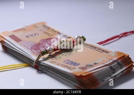 Raksha Bandhan festival Concept showing designer Rakhi or Wrist Band with scattered rice and kumkum,placed with Indian currency over colorful Stock Photo