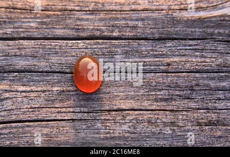 One isolated red orange chalcedony agate gemstone on wooden background shining in the sunlight. Chalcedony gems come in a variety of different colors