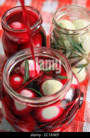 Marinated quail eggs in jars. Preparing quail eggs delicacy for Easter, with beetroot, vinegar, rosemary and pepper Stock Photo