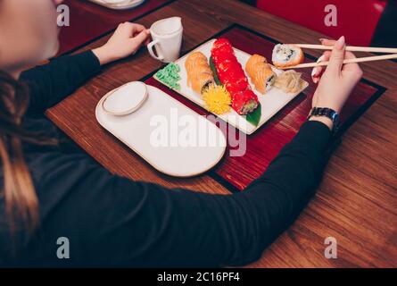 Eating sushi rolls with chopsticks. Japanese food in restaurant. Woman holds Philadelphia roll with chopsticks. POV shot Japanese Foods concept. Stock Photo