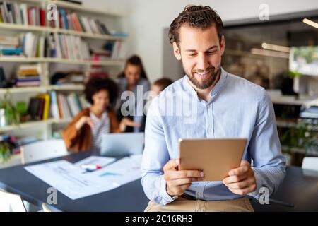 Smiling designer using his tablet pc while team works behind Stock Photo