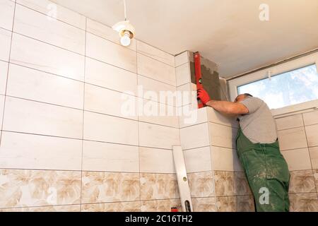Using a spirit level, the employee checks the plumb and evenness of the entire plane of the glaze placed on the bathroom wall. Stock Photo