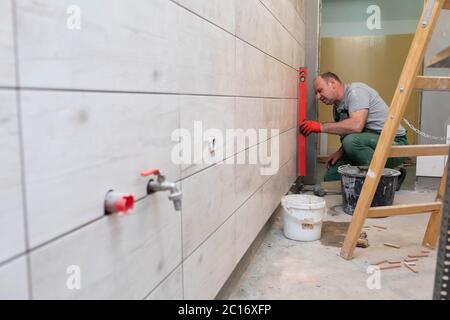 Using a spirit level, the employee checks the plumb and evenness of the entire plane of the glaze placed on the bathroom wall. Stock Photo