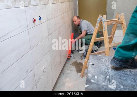 Using a spirit level, the employee checks the plumb and evenness of the entire plane of the glaze placed on the bathroom wall. Stock Photo