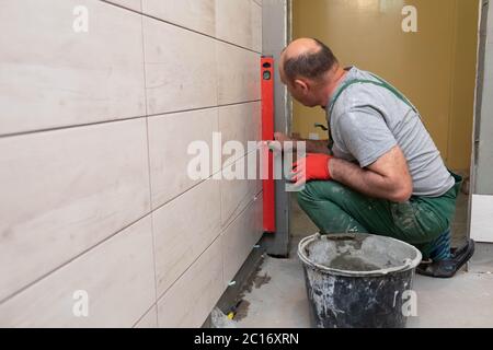 Using a spirit level, the employee checks the plumb and evenness of the entire plane of the glaze placed on the bathroom wall. Stock Photo