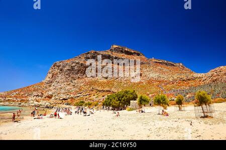 GRAMVOUSA - BALOS, THE CRETE ISLAND, GREECE - JUNE 4, 2019: The people are on the beach near the pirate castle mountain. Stock Photo