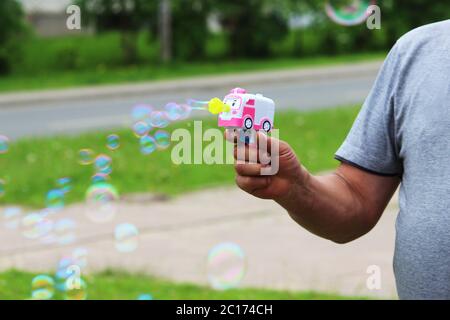 A big and cheerful man blows bubbles with a child's pistol. Stock Photo