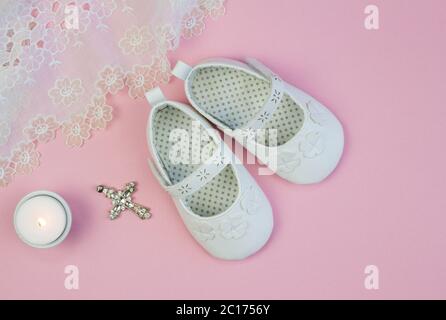 Pair of white baby booties on pink background with lace christening dress and candle Stock Photo