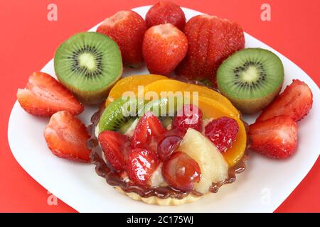 Cake with fruits kiwi, strawberries, raspberries, peach macro close up on white plate surrounded by fresh fruits Stock Photo