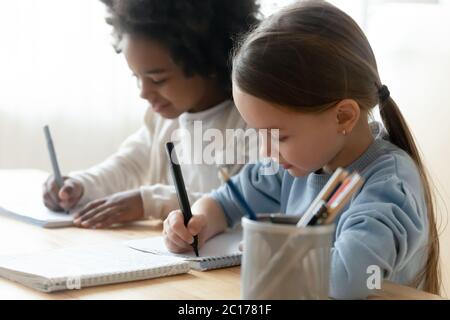 African and Caucasian schoolgirl mates sit at table writing task Stock Photo
