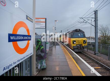 Colas rail Freight class 70 locomotive 70805 passing the London Overground roundel logo at Willesden Junction High level railway station. Stock Photo