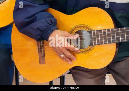 Approach to the hand of an elderly man sitting holding a guitar dressed in a blue shirt with a ring on his finger Stock Photo