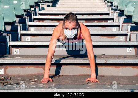 healthy fit woman doing sport at the stadium steps - woman doing workout wearing a protective mask Stock Photo
