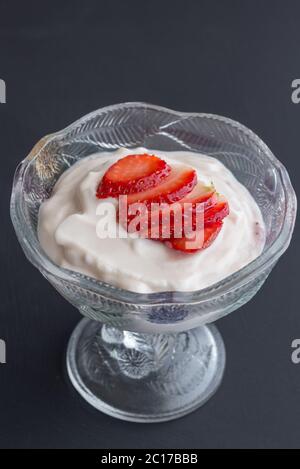 Yoghurt in glass bowl with cut strawberry topping isolated on black background Stock Photo