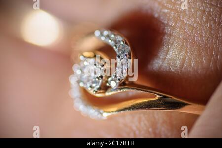 Macro shot of a golden diamond ring worn in finger. Human skin visible in the background Stock Photo