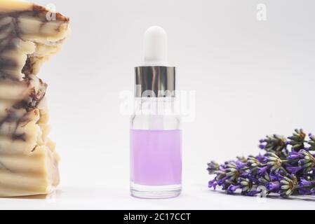 A glass dropper bottle with lavender oil and many beautiful lavender fresh flowers and handmade organic lavender soap near it on the light grey backgr Stock Photo