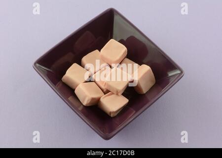 Strawberry toffee candy squares in purple candy bowl on lavender background Stock Photo