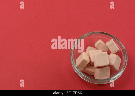 Strawberry toffee candy squares in glass candy bowl on red background Stock Photo
