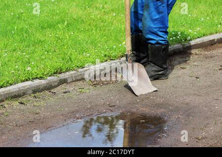 The worker removes the growing grass on a gravel path using an old shovel. Stock Photo