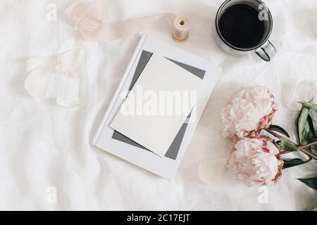 Wedding stationery, still life. Greeting card, invitation mockup scene. Bouquet of pink peonies flowers, cup of coffee and book on white linen table Stock Photo
