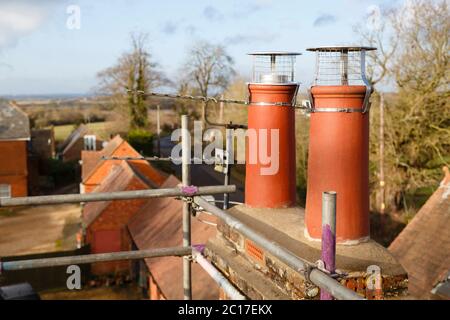 Clay chimney pot with cowl on a roof, repairing chimney with scaffolding UK Stock Photo