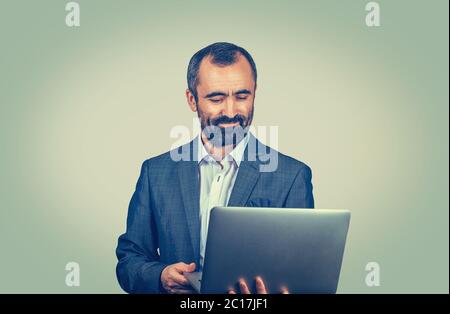 Young handsome mature middle age business man connecting to internet using looking attentively in a laptop. Mixed race bearded guy isolated on green s Stock Photo