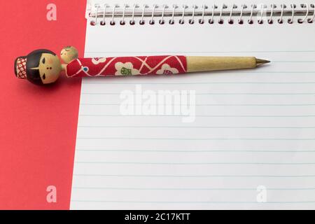 Figurine ball point pen on blank note pad with red background - Pen shaped as young Oriental woman w Stock Photo