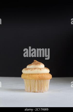 Cup cake background with single cupcake on white topped with cinnamon custard on rustic white with d Stock Photo