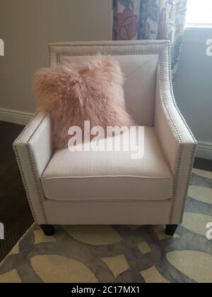 Bedroom interior with faux fur throw pillow on a white upholstered armchair Stock Photo