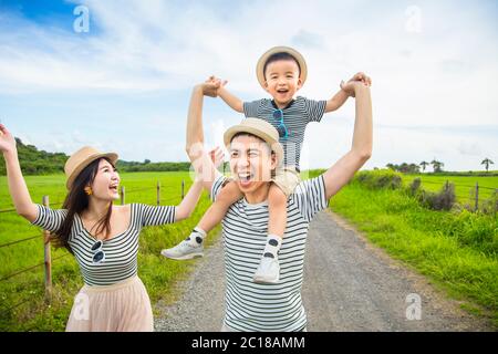 happy father giving son piggyback ride on his shoulders and walking on country road Stock Photo