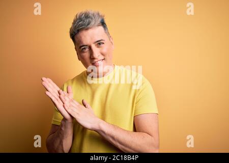 Young handsome modern man wearing yellow shirt over yellow isolated background clapping and applauding happy and joyful, smiling proud hands together Stock Photo