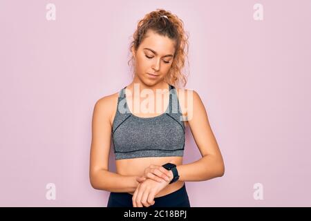 Young beautiful blonde sportswoman with blue eyes doing exercise wearing sportswear Checking the time on wrist watch, relaxed and confident Stock Photo