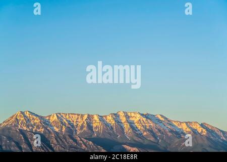 Rugged mountain with steep peaks covered with snow against vast blue sky Stock Photo