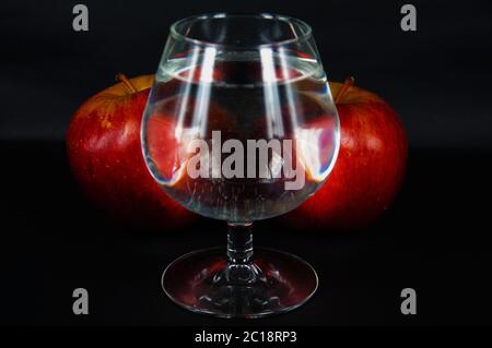 photo a glass of water and two red apples on a black background Stock Photo