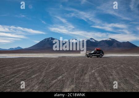 Truck driving through a desert with a lake and a volcano in the background and a blue sky Stock Photo